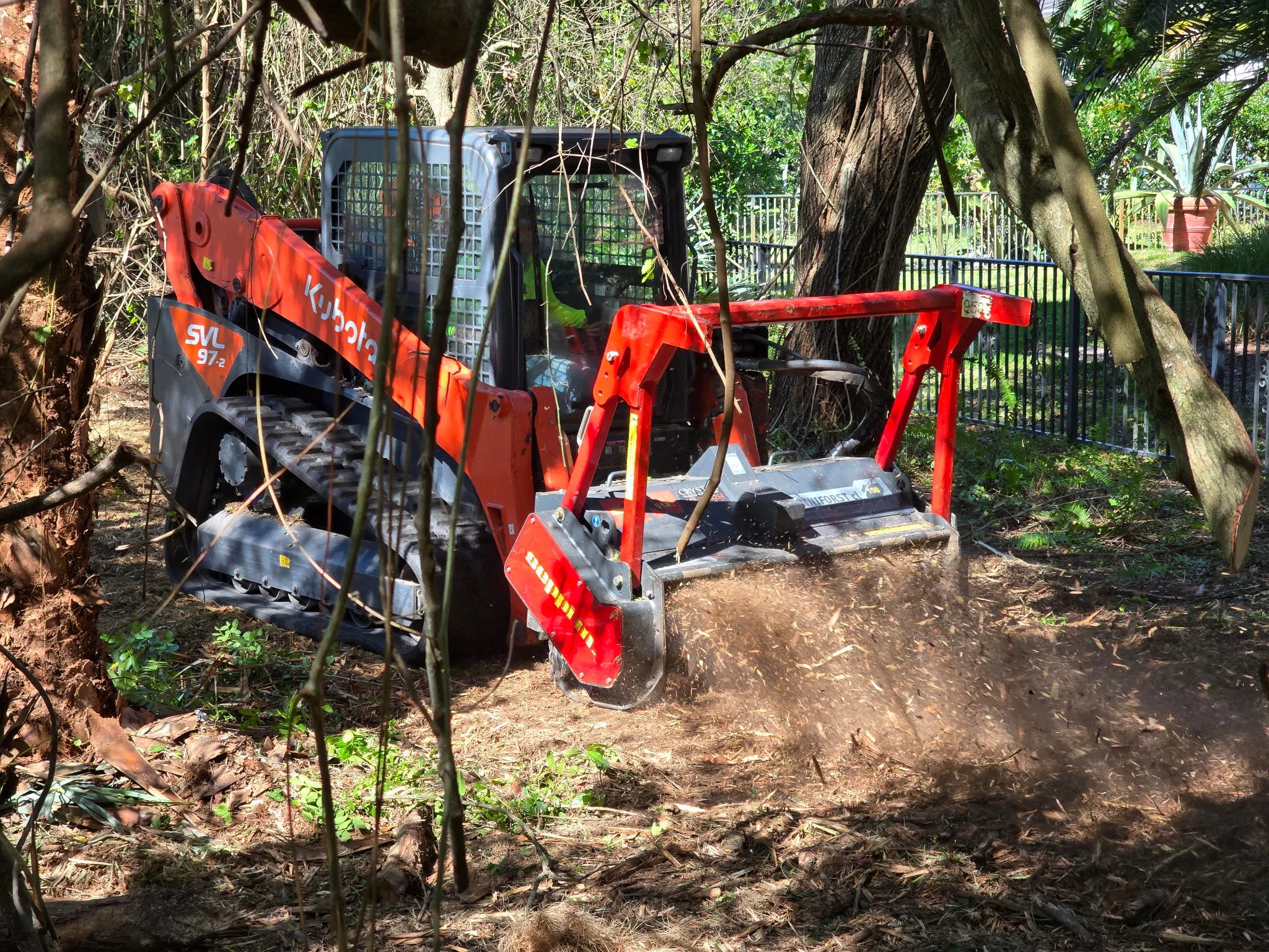 Skid steer moving through a brush clearing project with dust and open ground.